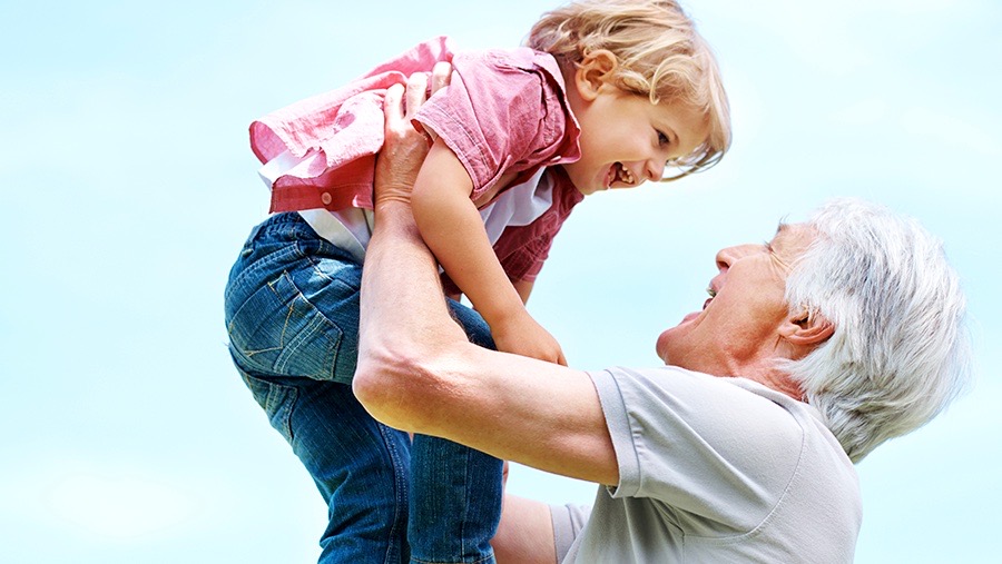 Grandfather holding up his granddaughter up in the air while both are smiling